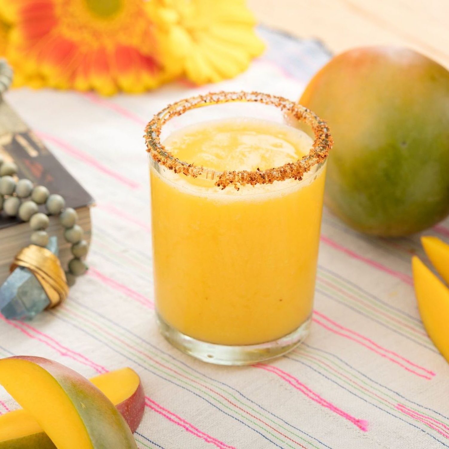 A glass of 21Seeds Frozen Mango-rita on a table with a mango and mango slices around the glass