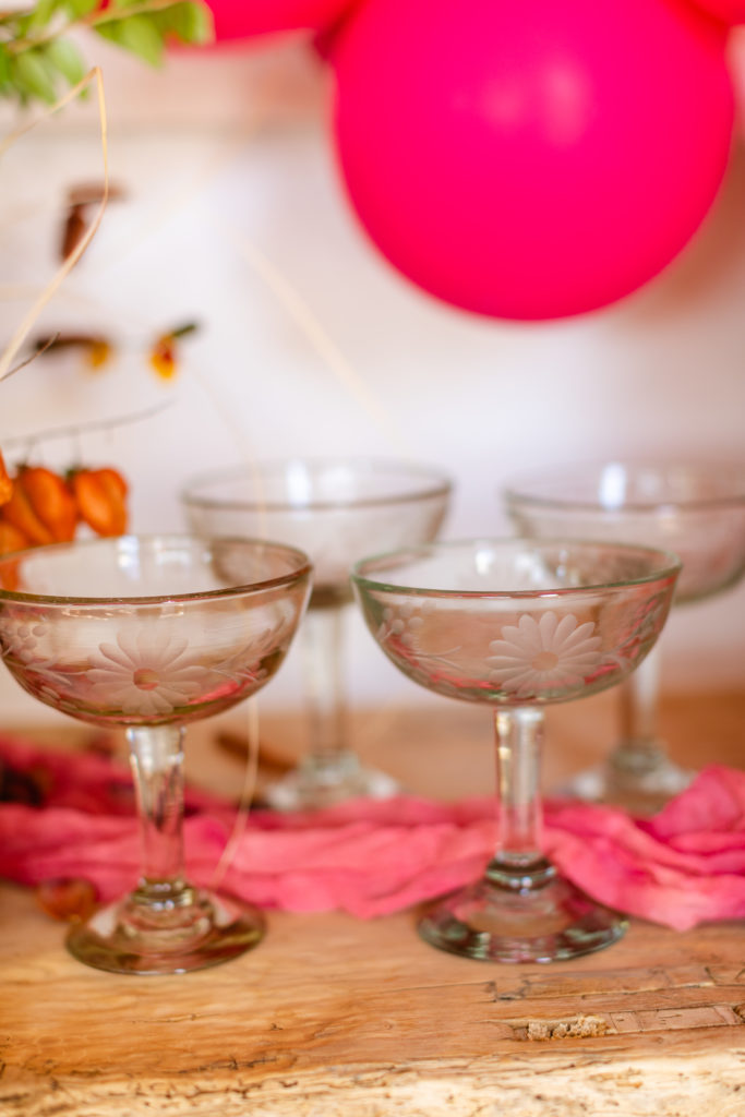 4 cocktail glasses on a tables with a balloon in the background.