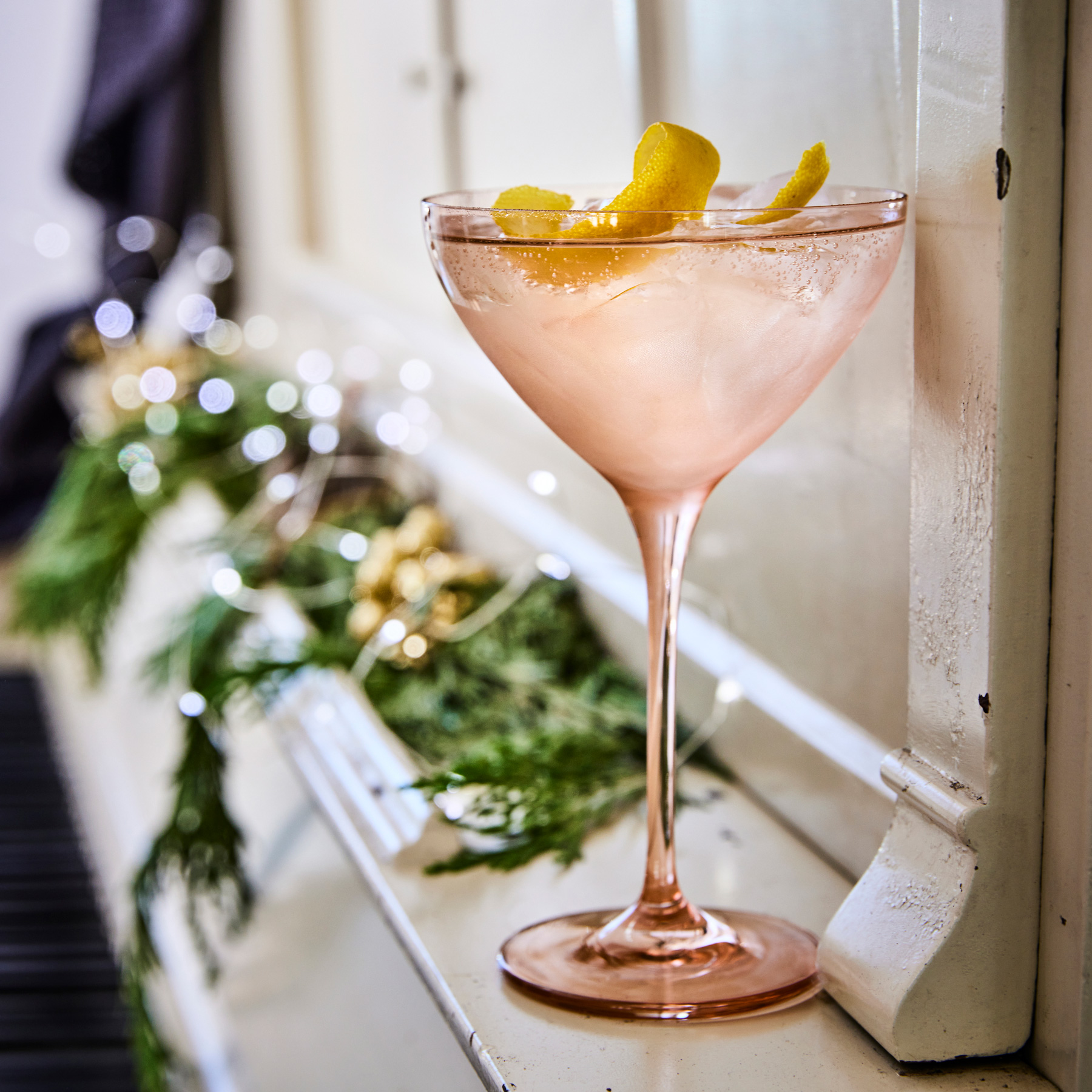 A cocktail in a pink glass garnished with a lemon swirl on a piano
